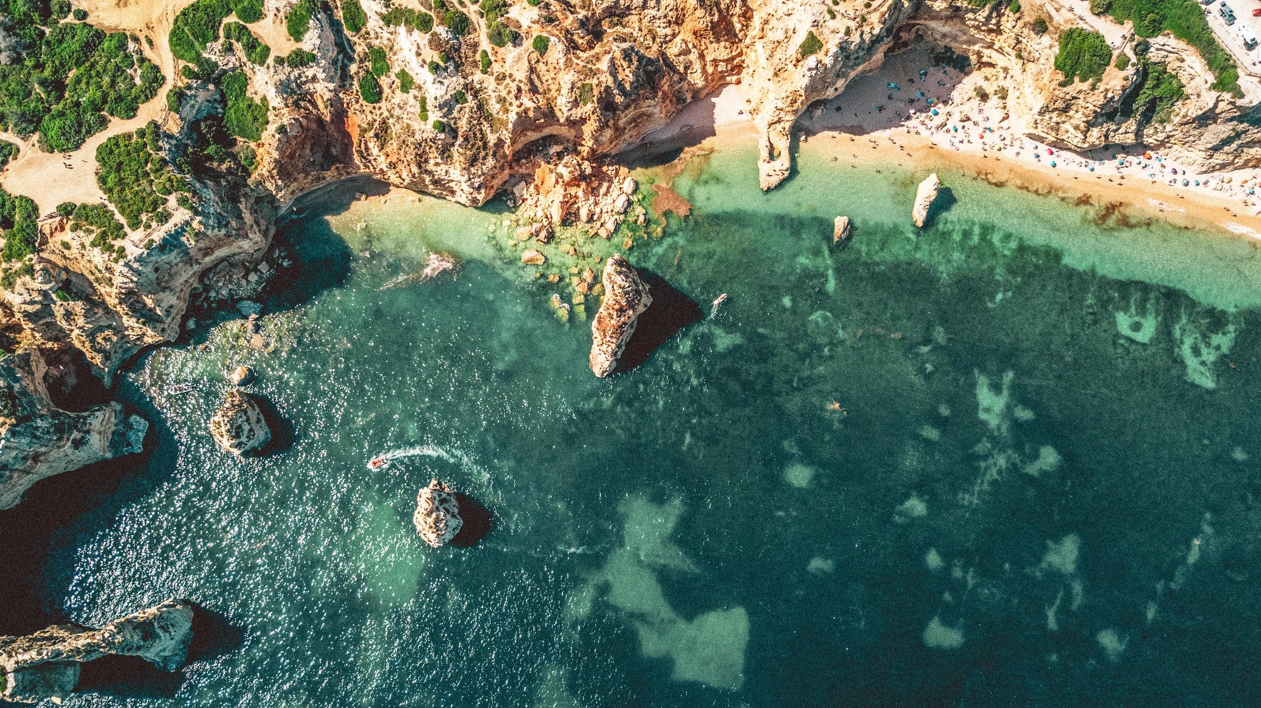 Vue de drone d'une plage paradisiaque avec plein de personnes et un bateau aux alentours des oliviers de Palombaggia en Corse-du-Sud.